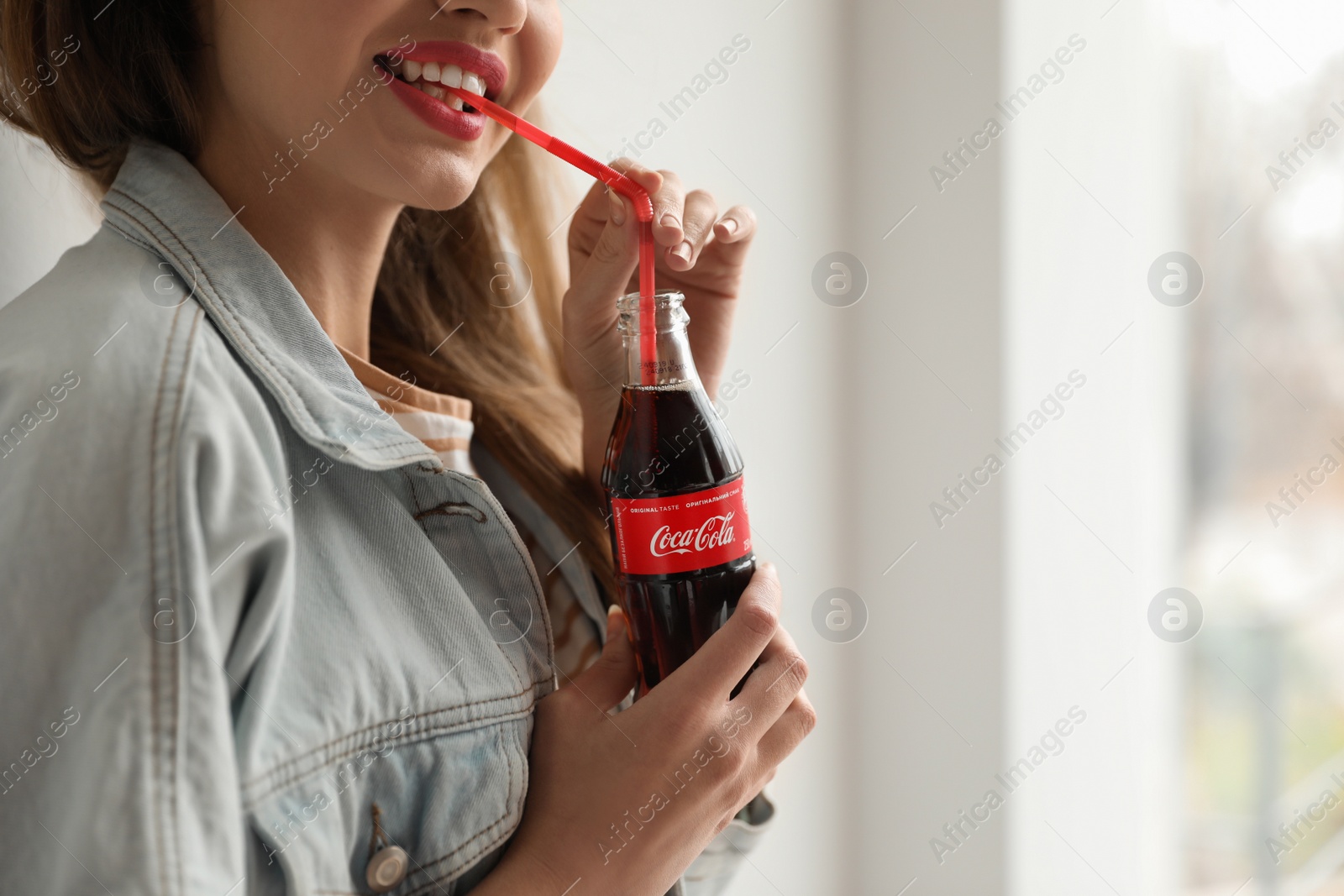 Photo of MYKOLAIV, UKRAINE - NOVEMBER 28, 2018: Young woman with bottle of Coca-Cola indoors, closeup. Space for text