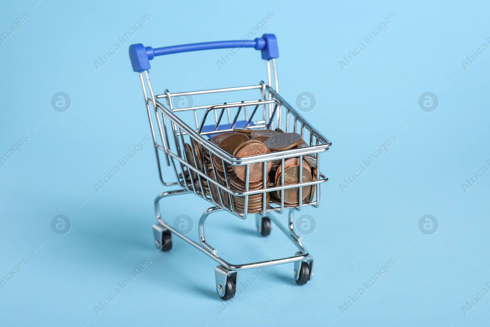 Photo of Small metal shopping cart with coins on light blue background