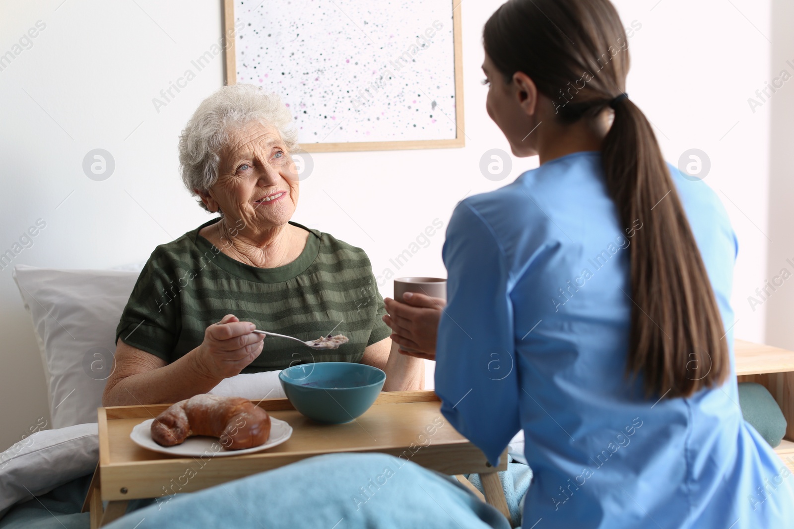 Photo of Care worker serving dinner for elderly woman in geriatric hospice