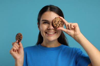 Young woman with chocolate chip cookies on light blue background