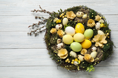 Decorative wreath with Easter eggs on white wooden background, top view