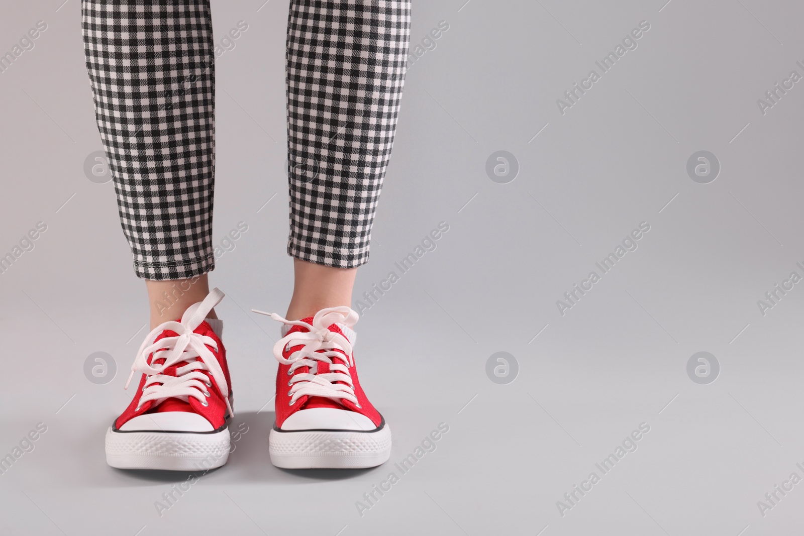 Photo of Woman wearing red classic old school sneakers on light grey background, closeup. Space for text