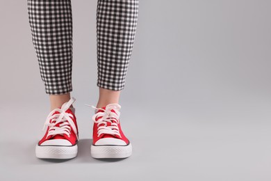 Photo of Woman wearing red classic old school sneakers on light grey background, closeup. Space for text