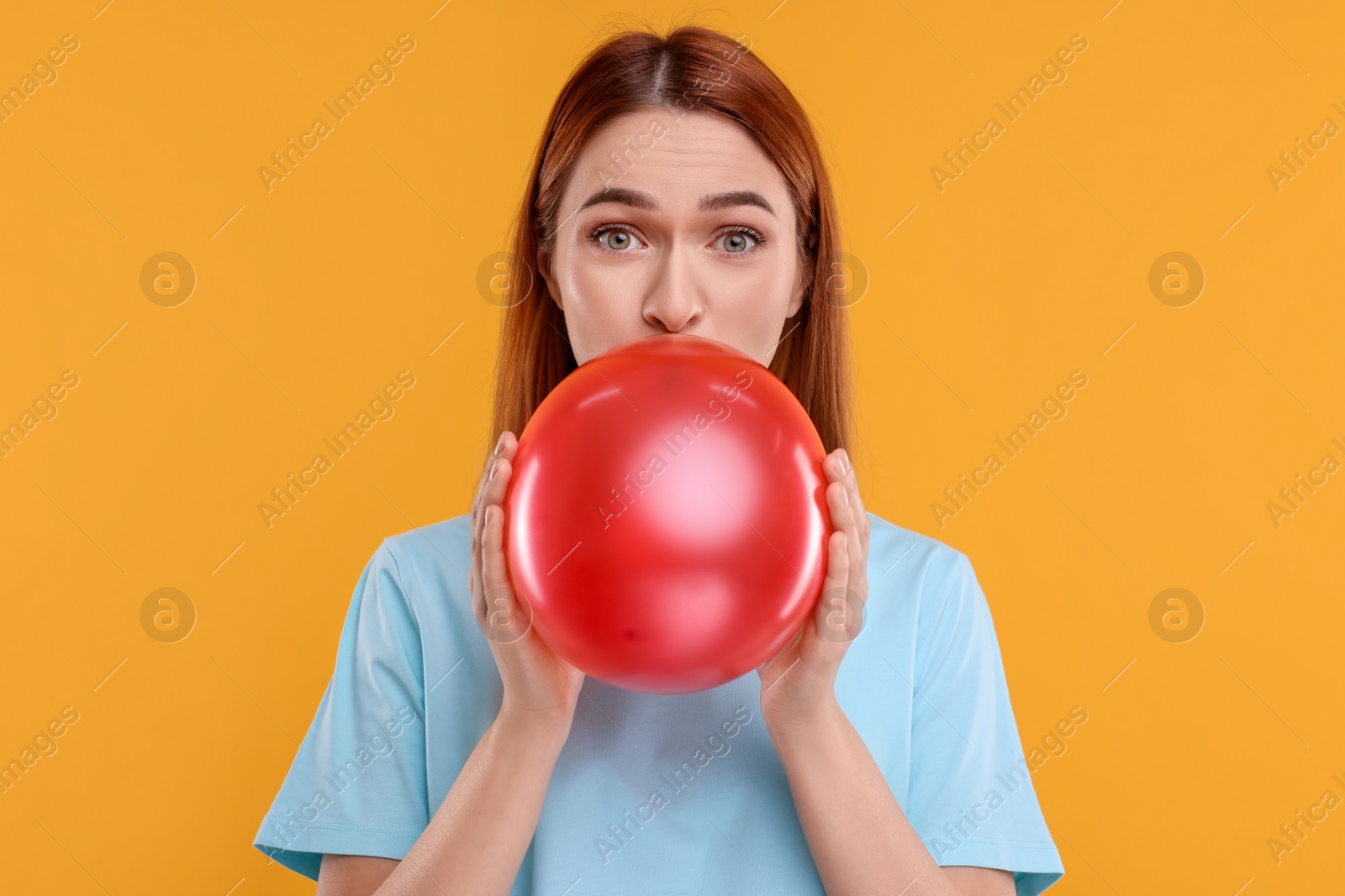 Photo of Woman inflating red balloon on orange background