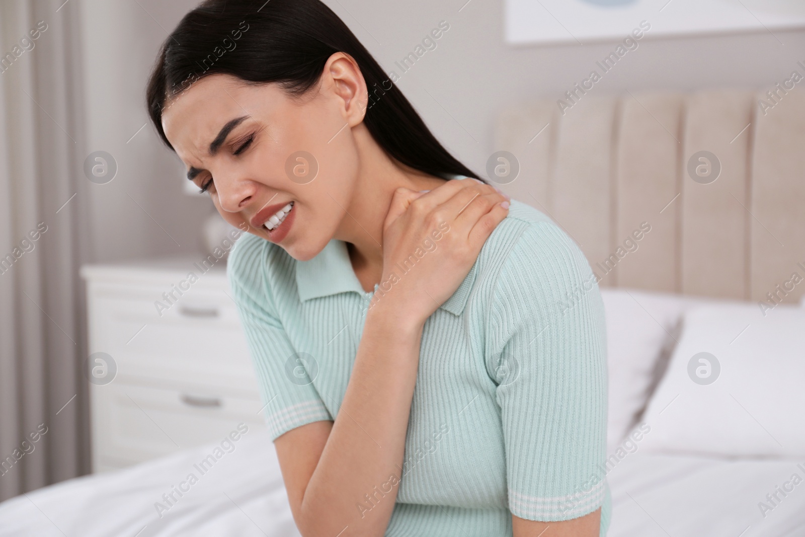 Photo of Woman suffering from shoulder pain on bed at home