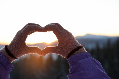 Photo of Woman making heart with her hands in mountains at sunset, closeup. Winter vacation