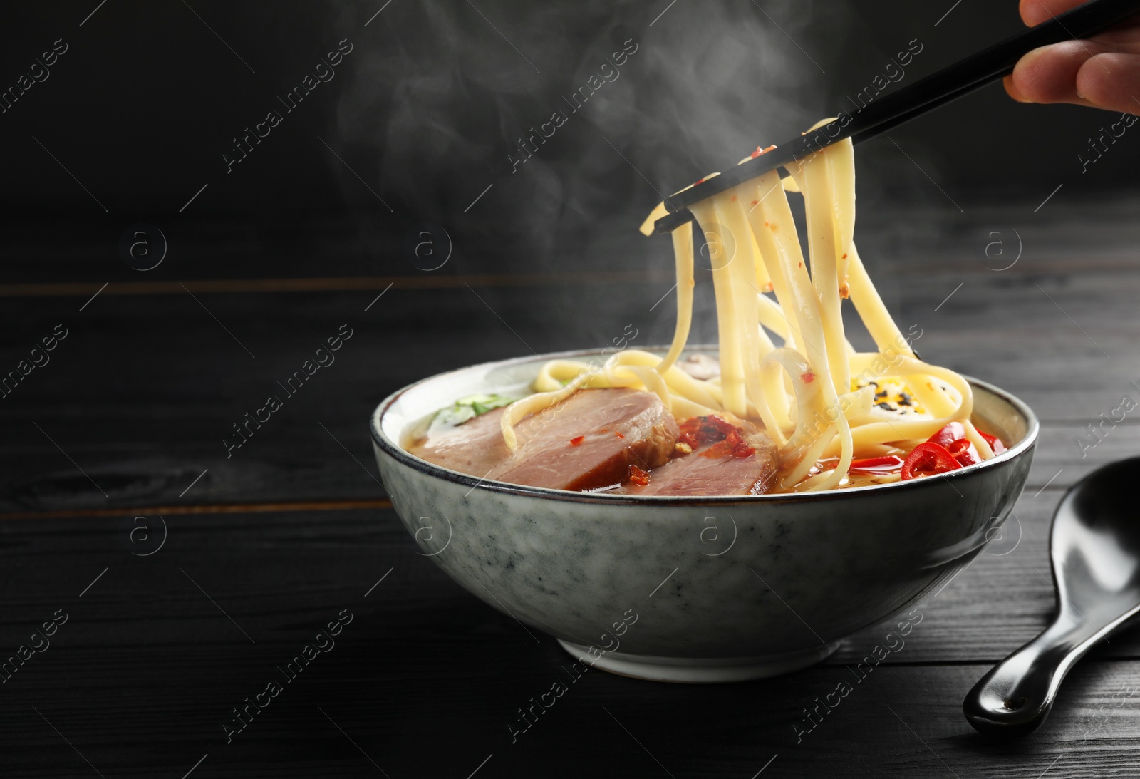 Image of Woman eating hot ramen with chopsticks at black wooden table, closeup and space for text. Noodle soup