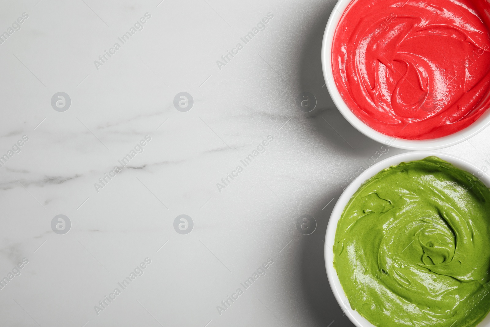 Photo of Bowls of different cream with food coloring on white marble table, flat lay. Space for text