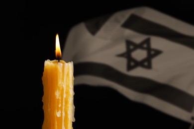 Image of Burning candle against flag of Israel on black background