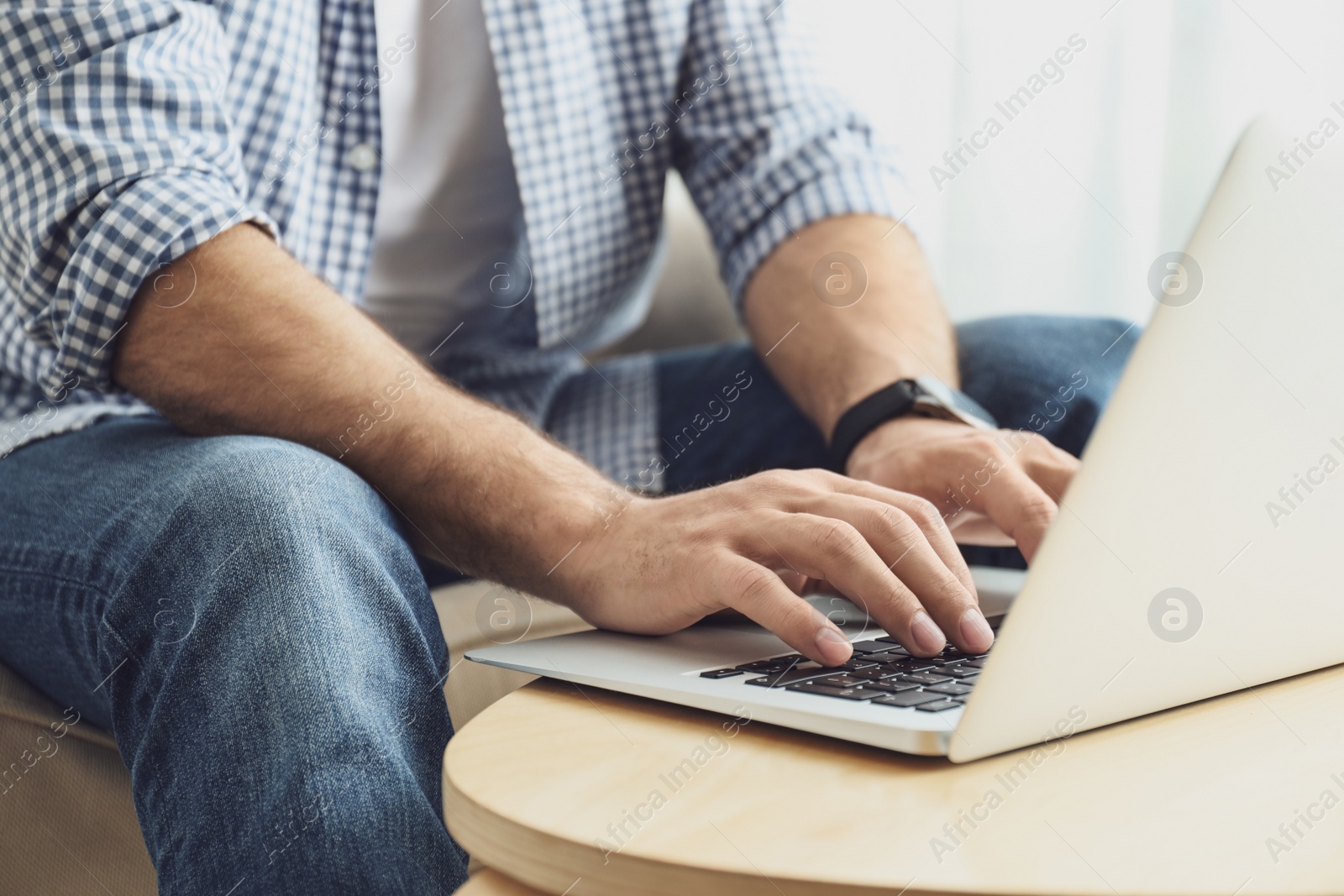 Photo of Man working on modern laptop at wooden table indoors, closeup