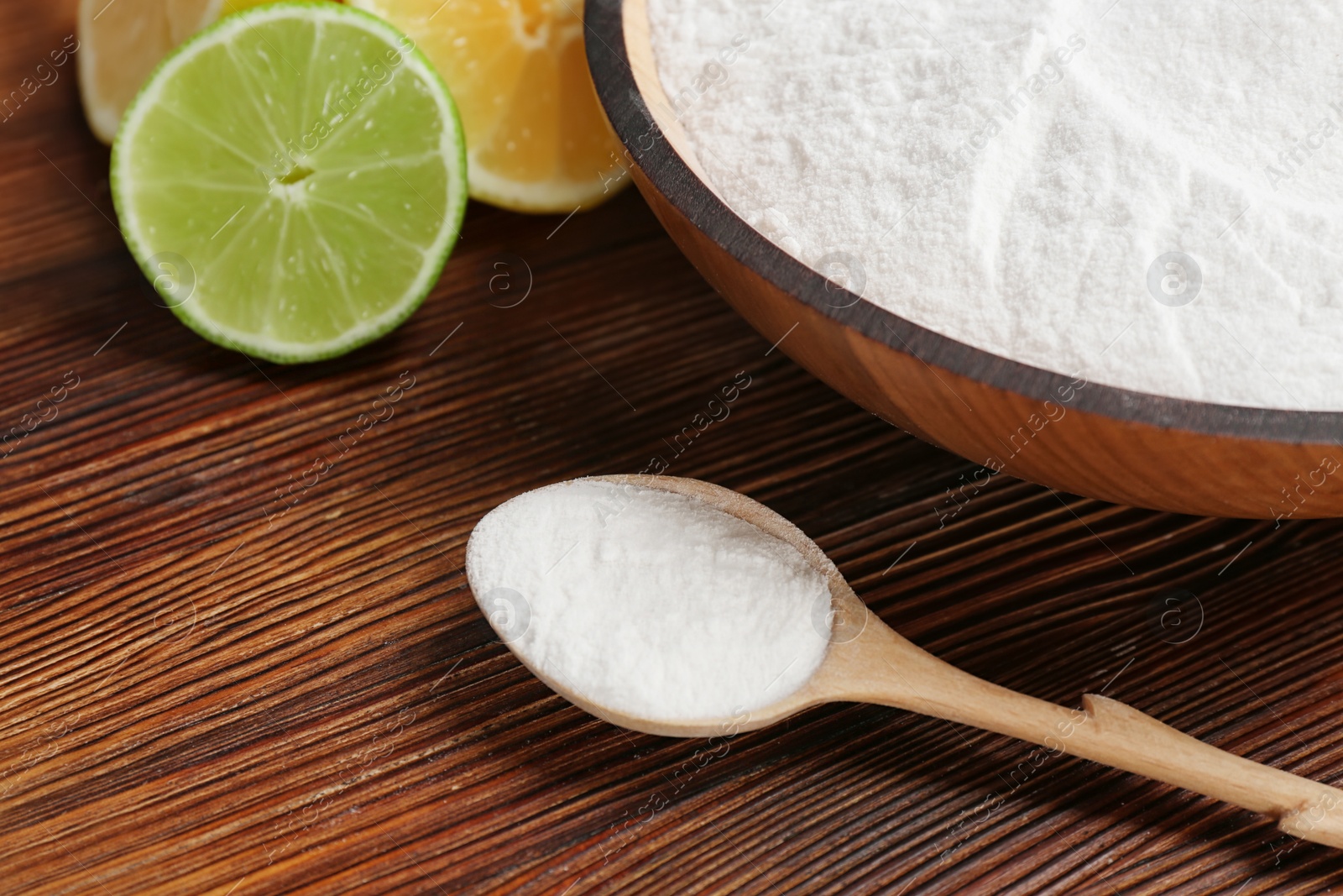 Photo of Spoon and bowl with baking soda on wooden table, closeup