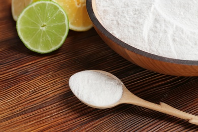 Photo of Spoon and bowl with baking soda on wooden table, closeup