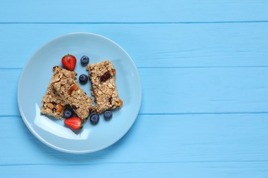 Photo of Tasty granola bars with berries on light blue wooden table, top view. Space for text
