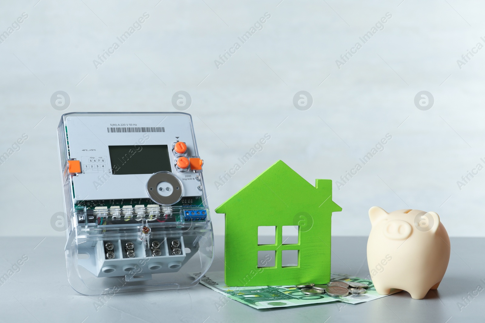 Photo of Electricity meter, piggy bank and euro banknotes on grey table