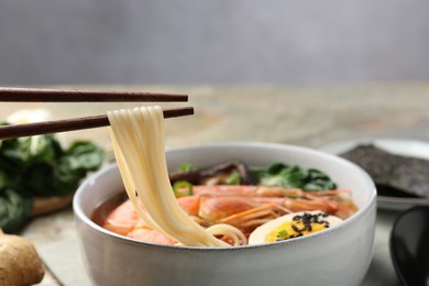 Eating delicious ramen from bowl with chopsticks at table, closeup. Noodle soup
