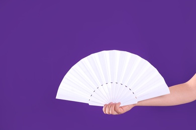 Woman holding white hand fan on purple background, closeup