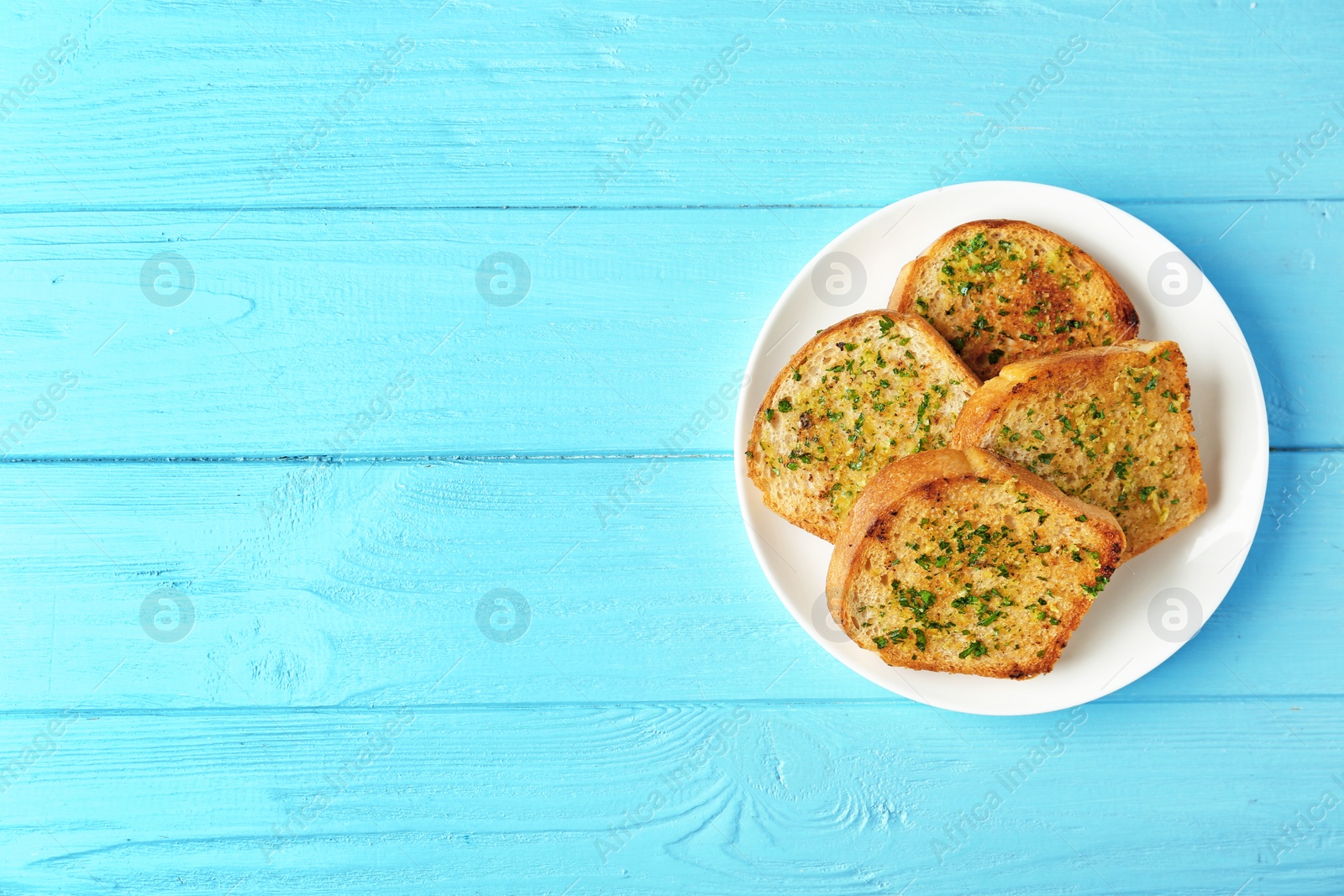 Photo of Slices of toasted bread with garlic and herbs on blue wooden table, top view. Space for text