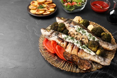 Photo of Plate with delicious baked sea bass fish and sauce on dark table. Space for text