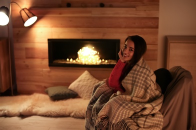 Young woman resting near decorative fireplace at home. Winter season