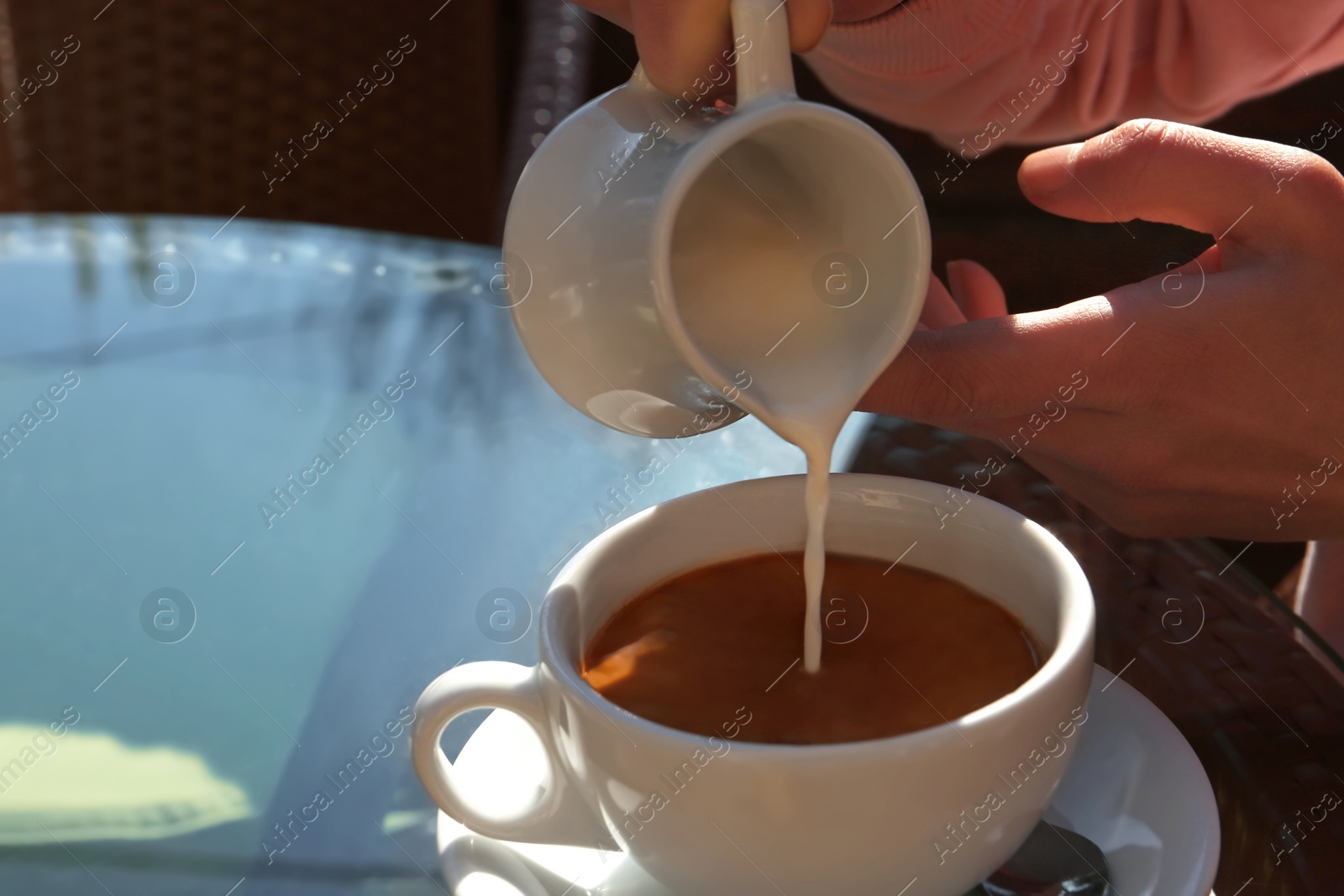 Photo of Woman pouring milk in coffee at table in cafe