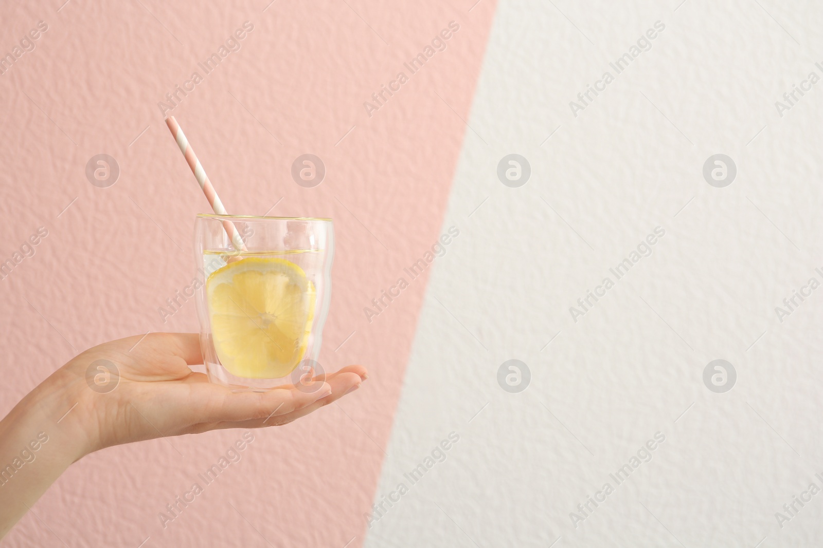 Photo of Young woman holding glass with lemon water against color background