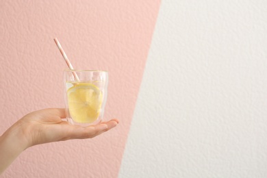 Photo of Young woman holding glass with lemon water against color background