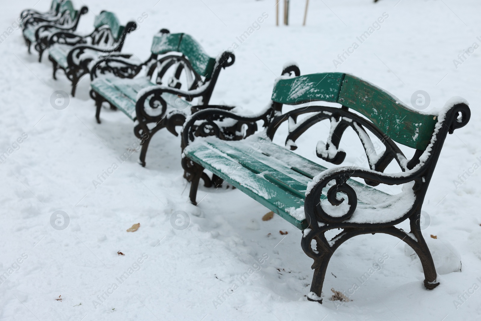 Photo of Green wooden benches covered in snow outdoors