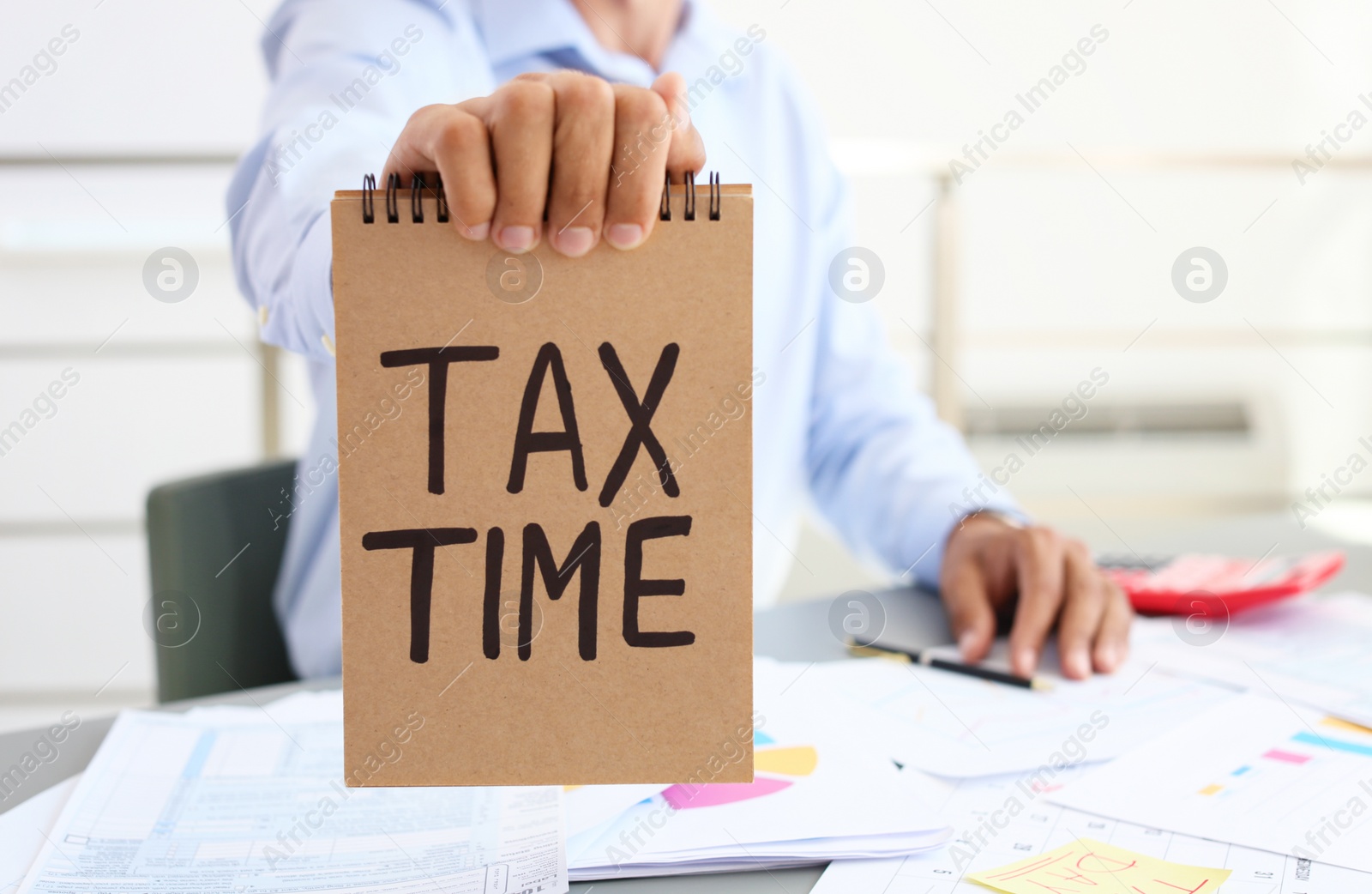 Photo of Man holding notebook with words TAX TIME indoors