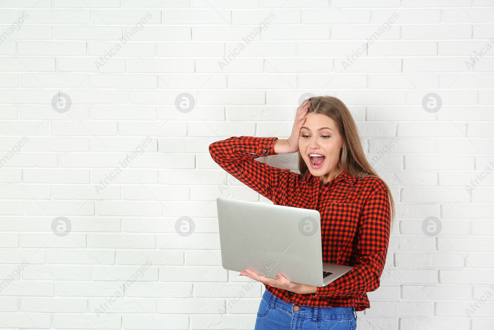 Photo of Emotional young woman with laptop celebrating victory near brick wall. Space for text