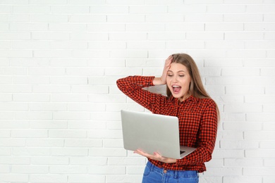 Photo of Emotional young woman with laptop celebrating victory near brick wall. Space for text