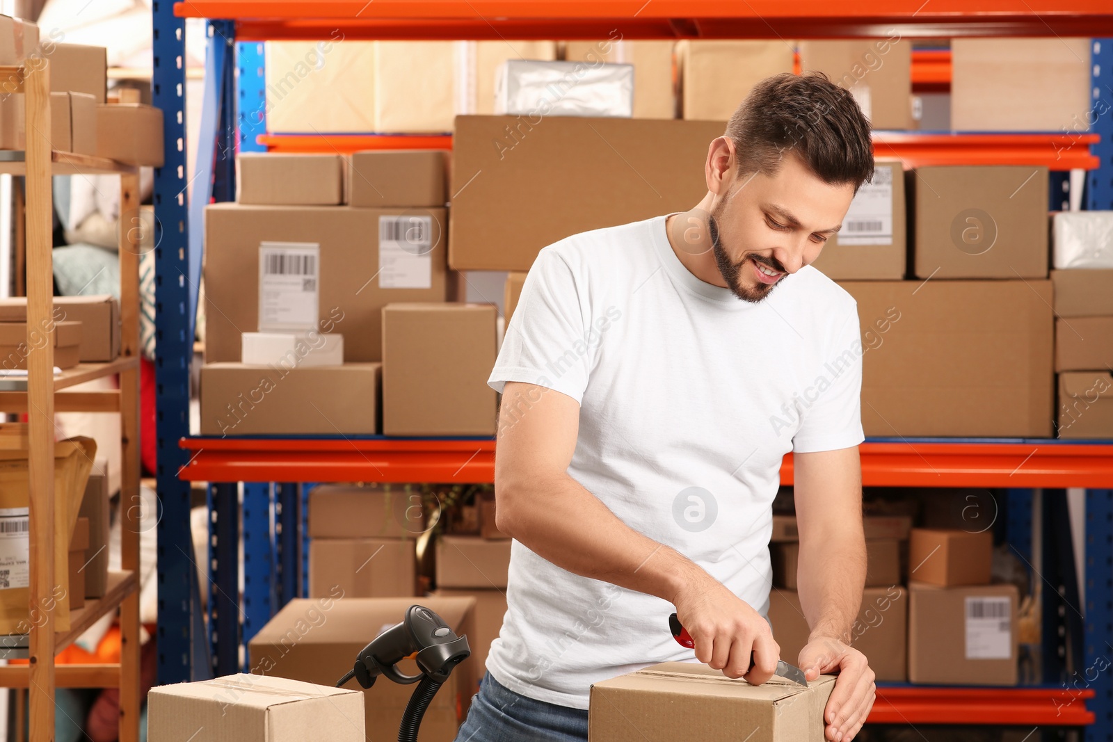 Photo of Post office worker with utility knife opening parcel indoors