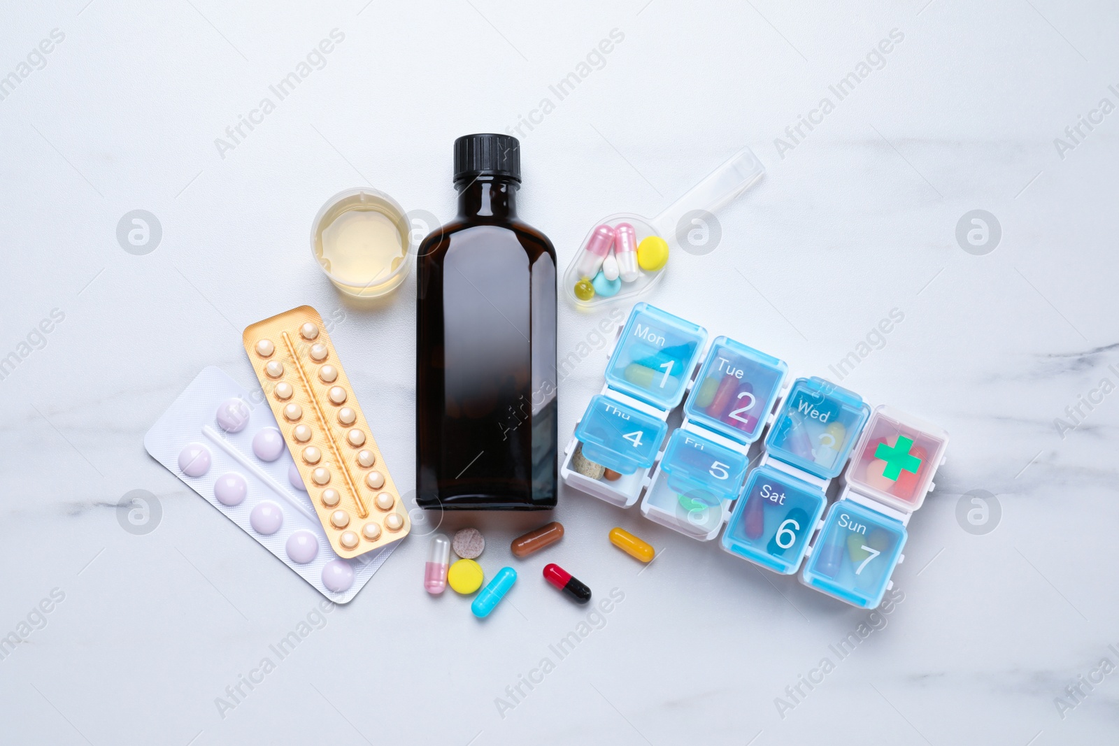 Photo of Bottle of syrup, measuring cup, dosing spoon and pills on white marble table, flat lay. Cold medicine