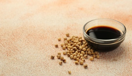 Photo of Soy sauce in bowl and beans on beige textured table, closeup. Space for text
