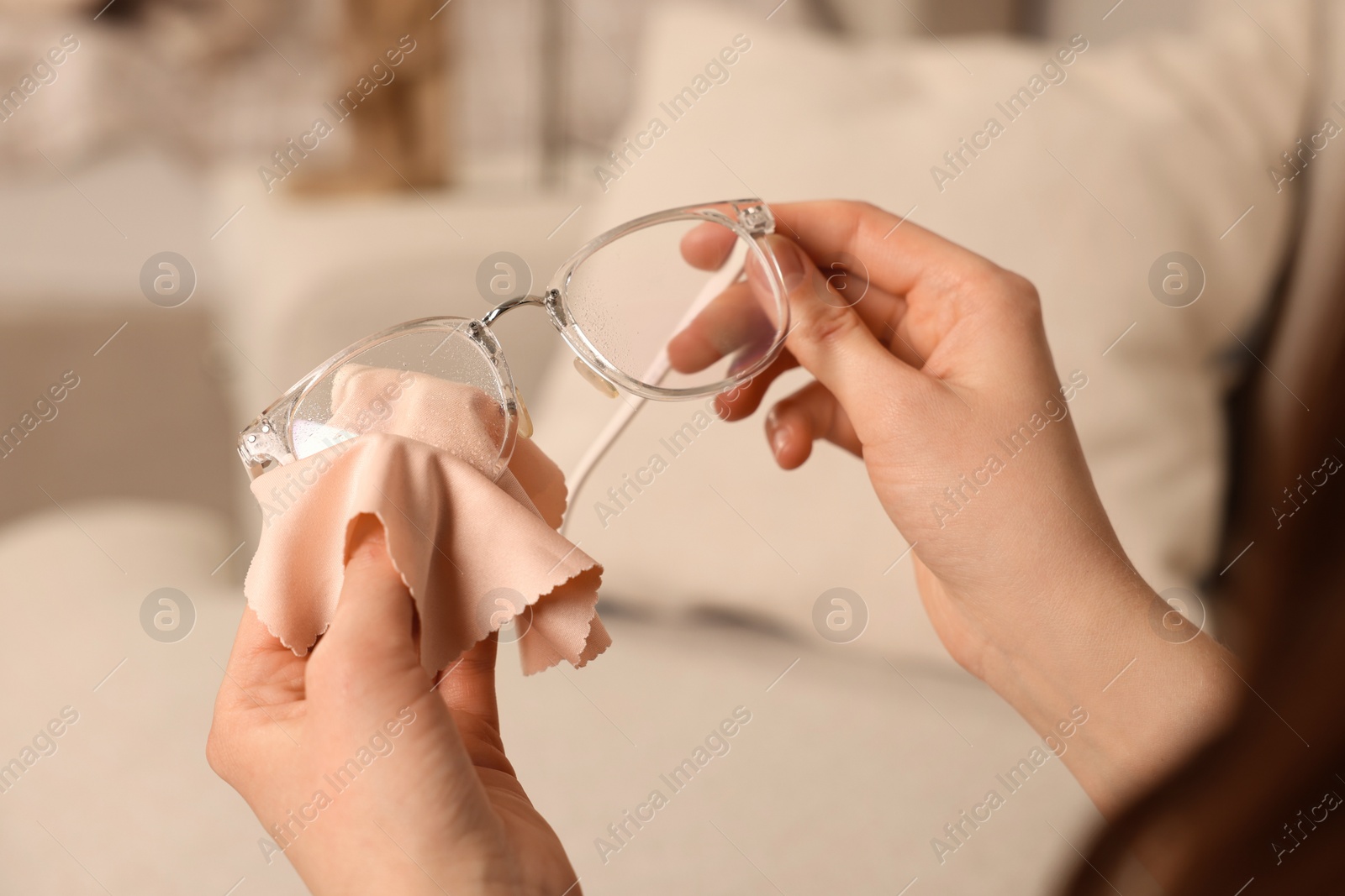 Photo of Woman cleaning glasses with microfiber cloth at home, closeup