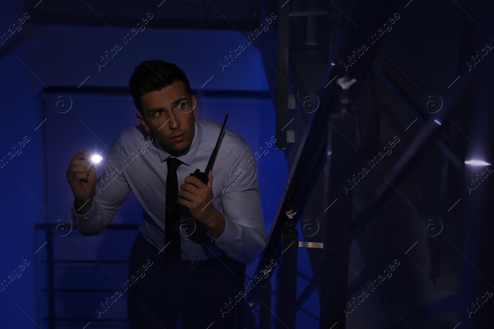 Photo of Male security guard with flashlight and portable radio transmitter in dark room