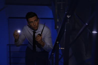 Photo of Male security guard with flashlight and portable radio transmitter in dark room