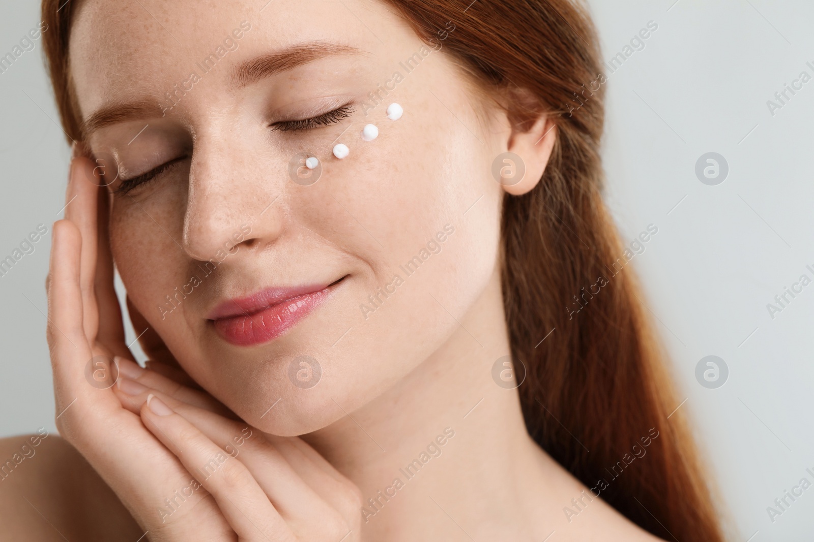 Photo of Beautiful woman with freckles and cream on her face against grey background, closeup