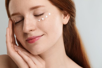 Beautiful woman with freckles and cream on her face against grey background, closeup