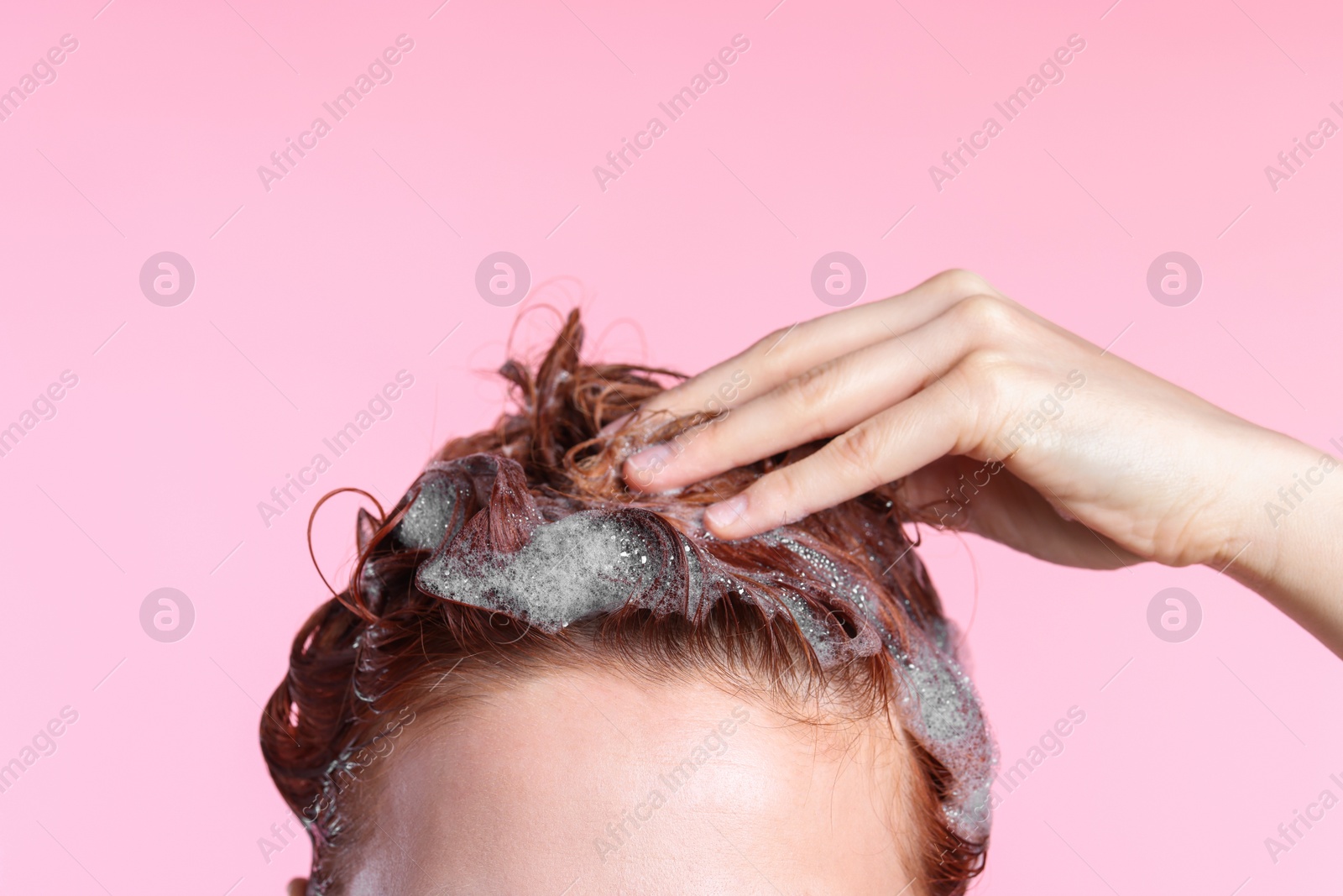 Photo of Young woman washing her hair with shampoo on pink background, closeup. Space for text