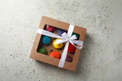 Box with delicious colorful cupcakes and confetti on light grey table, flat lay
