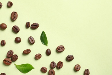 Fresh green coffee leaves and beans on light green background, flat lay. Space for text