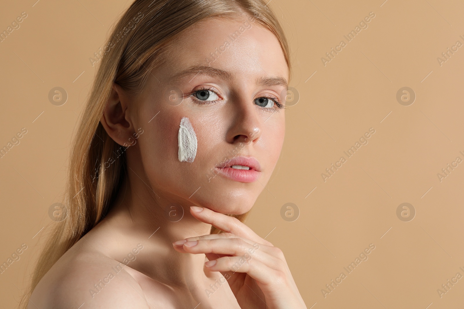 Photo of Beautiful young woman with sun protection cream on her face against beige background, space for text