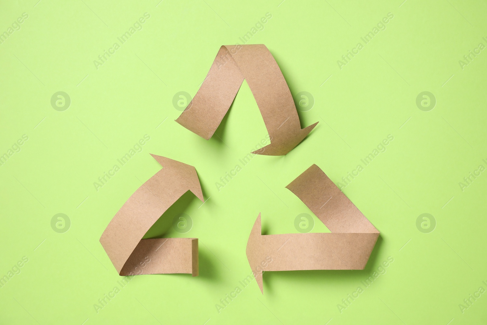 Photo of Recycling symbol cut out of paper on green background, top view