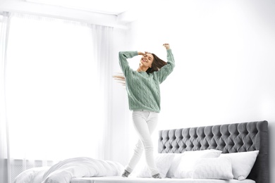 Photo of Young woman in warm sweater jumping on bed at home
