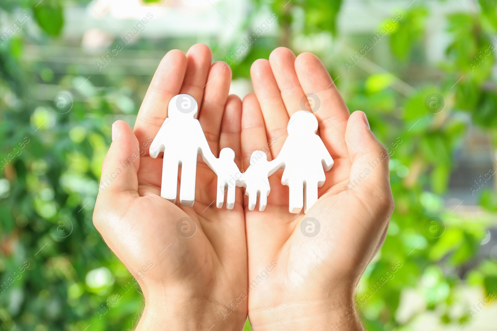 Photo of Young man holding wooden family figure in his hands against blurred background, closeup