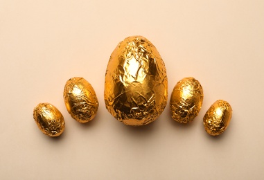 Photo of Chocolate eggs wrapped in golden foil on beige background, flat lay