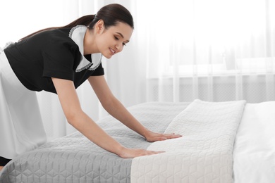 Young maid making bed in hotel room. Space for text