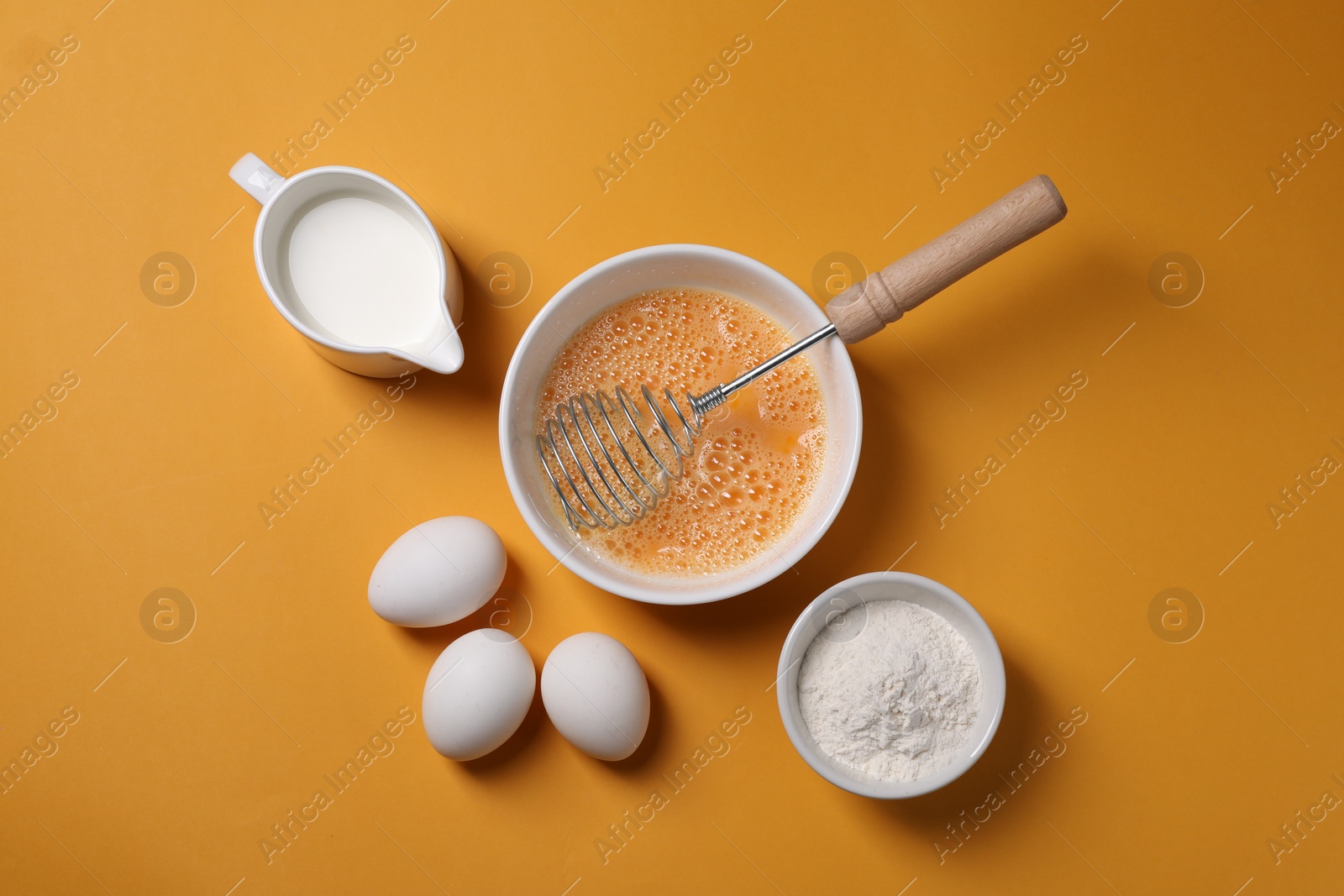 Photo of Making dough. Beaten eggs in bowl, flour and milk on orange background, flat lay