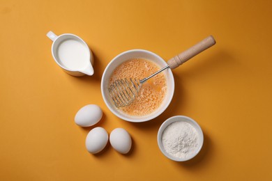 Making dough. Beaten eggs in bowl, flour and milk on orange background, flat lay