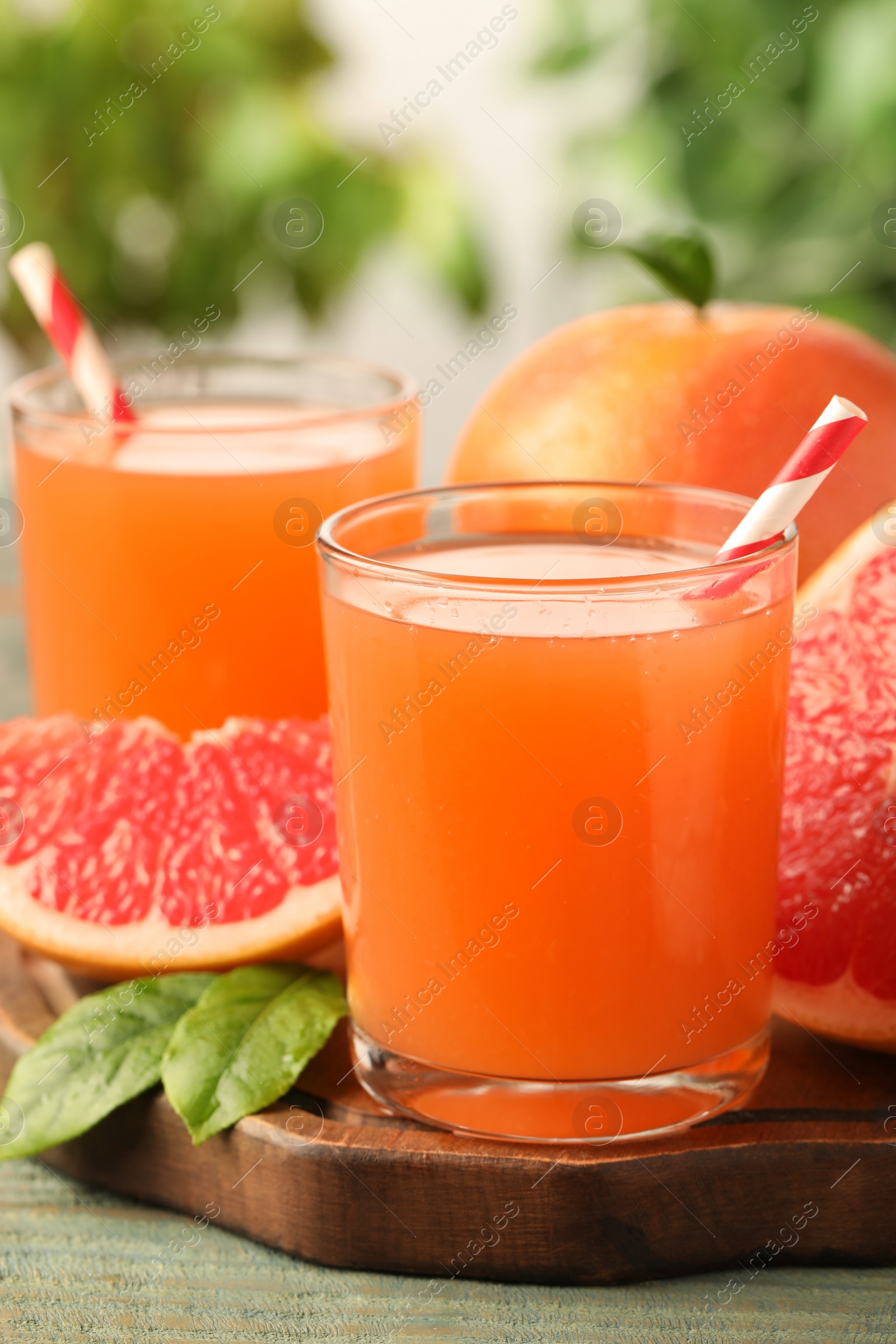 Photo of Glasses of delicious grapefruit juice on wooden table against blurred background